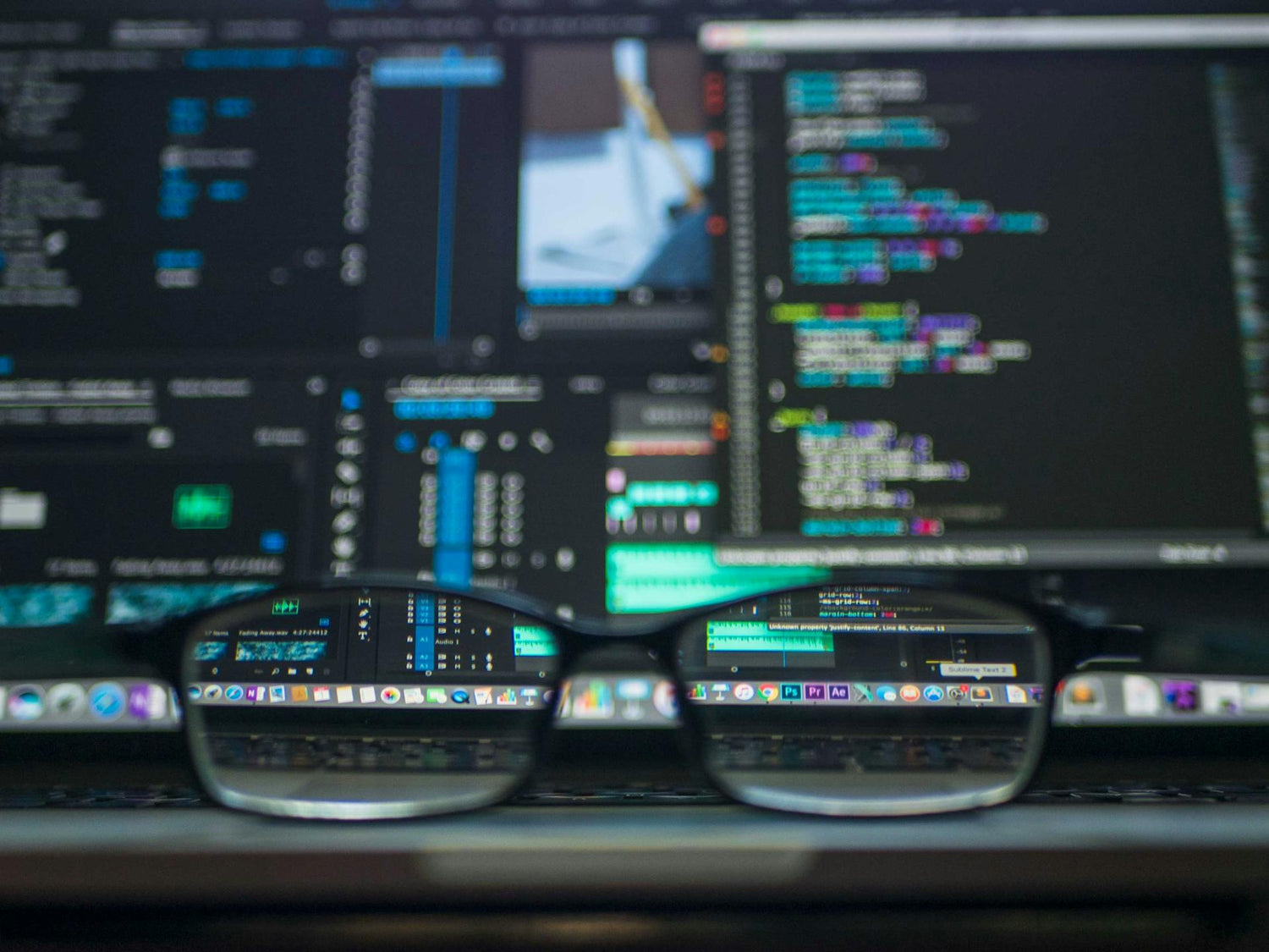 Picture of glasses on a desk in front of a computer screen with coding to symbolize technology transformation via software and hardware development including websites, digital marketing, ecommerce, consumer electronics, and other development